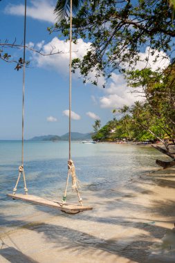 Tropik kumlu sahil suyunun üzerinde sallanan ahşap salıncak, Koh Chang, Tayland