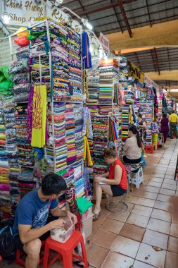 İnsanlar renkli kumaş yığınlarının arasından alışveriş yapıyorlar.