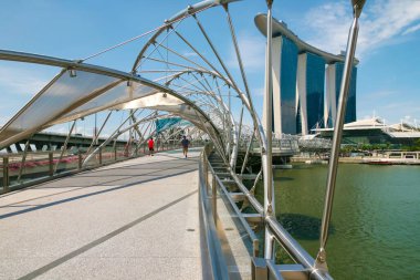 Erkekler ve kadınlar Helix Köprüsü 'nde Marina Bay Sands otelinin arka planında yürüyorlar. Singapur