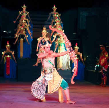 Bir grup özenle hazırlanmış destansı kostümlü erkek dansçı karanlık bir sahnede gösteri yapıyor. 