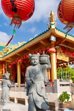 Phuket tapınağındaki renkli fenerlerin yanındaki taş heykeller.