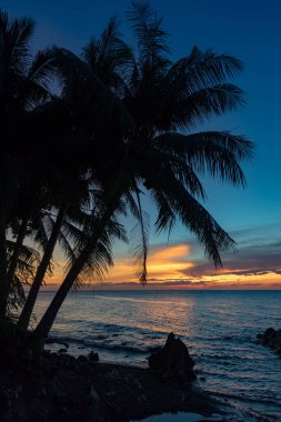 Parlayan ufuk ve sakin deniz dalgalarıyla huzurlu ve canlı bir akşam, kıyıda, Camiguin, Filipinler