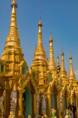 Açık mavi gökyüzünün altında detaylı oymalarla süslenmiş altın ve beyaz şapşallar. Myanmar.