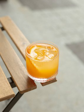 Ahşap masanın köşesinde portakal dilimli ve buzlu kokteyl.