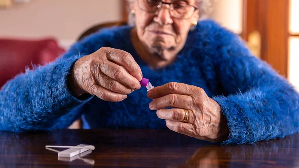 Old woman open a sample for covid-19 antigen diagnostic test device at home. Caucasian grandma using set with cassette kit for self testing to check the infection of Coronavirus. Grandmother quarantine pandemic.