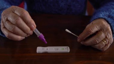 Kafkas büyükannesinin, evdeki koronavirüsü tespit etmek için numuneyi tampon damlatıcıya yerleştirdiği yakın plan. Büyükannem PCR testini kalabalıktan döndükten ve insanlarla tanıştıktan sonra kullanıyor. Yaşlı kadın.