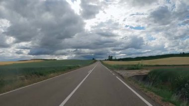 Driving car on empty regional road through the fields outside the city during sunny day in Spain. Countryside asphalt road landscape scene. Traffic ways transportation logistics and traveling concept