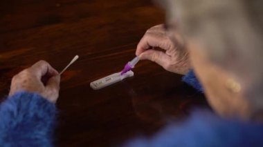 Yaşlı kadın numuneyi evdeki covid-19 antijen test cihazına yerleştiriyor. Kafkasyalı büyükanne Coronavirus enfeksiyonunu kontrol etmek için kaset setini kullanıyor..