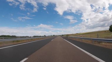 Empty highway road through the fields outside the city during sunny day. Two way asphalt road with country views with scattered and low clouds at Spain. Traffic ways transportation logistics concept.