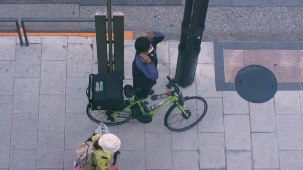 2023年4月13日 日本13日 Uber自転車の隣に立っているデリバリーマンのスローモーション空中ビューが次の順序を満たす準備ができています 歩道に自転車を持った配達制服の人 — ストック動画