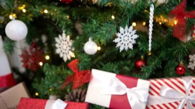 Modern bir Noel ağacının altında, zarif bir şekilde paketlenmiş hediye kutuları, yeni yıl dekorasyonu için bir tasarım unsuru olarak, Noel süslerinin yanı sıra beyaz arka planlı bir evde tatil atmosferini artırır..