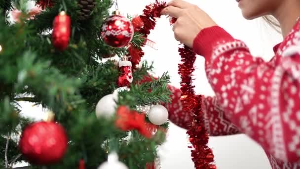 メリークリスマスとハッピーな休日 アジアの女性の手は冬に家で屋内でタンクガーランドでスプルースの木を飾っています 装飾のための火の枝のXmasボール掛かる — ストック動画