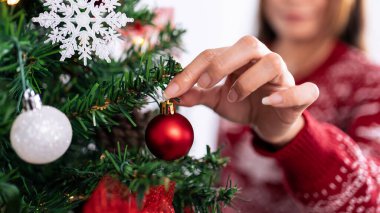 Oturma odasında kırmızı toplarla Noel ağacı süsleyen bir kadın. Mutlu Noeller ve mutlu yıllar konsepti. Kız ladin dallarına Noel süsleri takıyor. Aile sıcacık anları