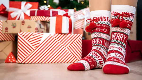 A young girl with warm socks and copy space. Woman enjoys the winter season in the comfort of her home and a box of surprise gifts by Christmas tree, creating a happy and cozy holiday celebration