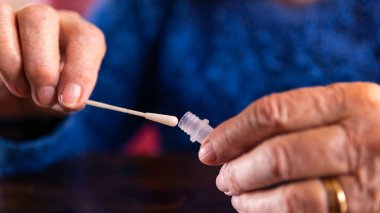 Kovid19 için antijen teçhizatıyla kendi kendine test yapan yaşlı bir kadının yakın çekimi. Kafkasyalı büyükanne Coronavirus enfeksiyonunu kontrol etmek için tampon damlatıcıya burun çubuğu takıyor..