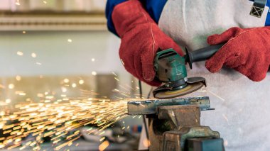Worker grinding metal with a grinder and cleaning the steel seam. Working in a metal processing workshop. The man works with an electric tool. Sparks from metal heating.