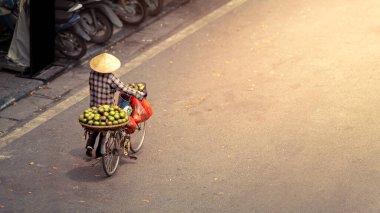 Geleneksel Asya konik hasır şapkası takan Vietnamlı bir kadının hava görüntüsü, Hanoi caddesinde satmak için yeşil meyvelerle bisiklete biniyor ve boş fotokopi alanı var. Vietnam