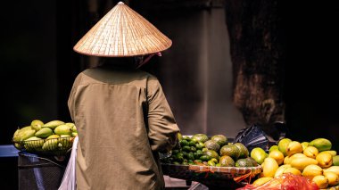 A Vietnamese street vendor wears a classic Asian conical straw hat while offering an assortment of tropical fruits on her bicycle. Vietnam cultural heritage, traditional charm of street commerce city clipart