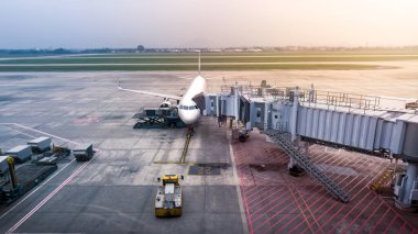 Gün batımında bir Boeing uçağı uluslararası havaalanında yolcu almaya hazır. Bir uçak kalkış terminalinde yolcuları bekliyor, yaklaşan uçuş için hazırlanıyor..