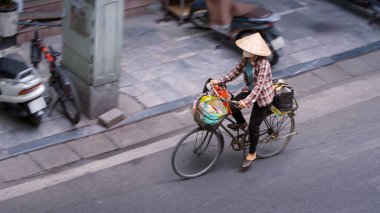 Vietnam Hanoi Eski Mahallesi 'ndeki hava manzarası, geleneksel Asya konik hasır şapkalı bir kadın, ıssız bir cadde boyunca bisiklet sürüyor. Vietnam kültür mirasını ve yerel kültürü temsil ediyor.