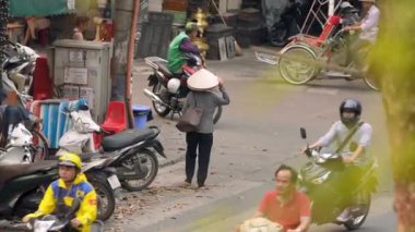 Vietnam, -03 Nisan 2024: Vietnamlı bir kadın sokak satıcısının ağır çekimde Hanoi Eski Mahallesi 'nde geleneksel Asya konik hasır şapkası ve sembolik kültür mirası takmış bir yolda yürüyor.