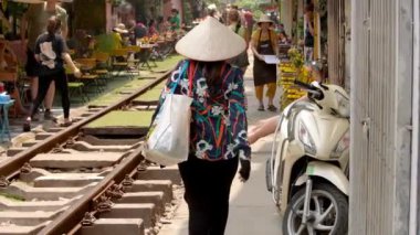 Vietnam, -01 Nisan 2024: Vietnamlı bir kadının yavaşlığı Old Quarter 'daki ünlü tren yolu boyunca yürüyor, geleneksel Asya konik hasır şapkası takıyor, sembolik kültür mirası.