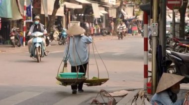 Vietnam, -03 Nisan 2024 Hanoi Eski Mahallesi 'nde bir cadde boyunca yürüyen Vietnamlı kadının yavaşlaması, geleneksel Asya konik hasır şapkası takıyor, Vietnam kültür mirasının simgesi..