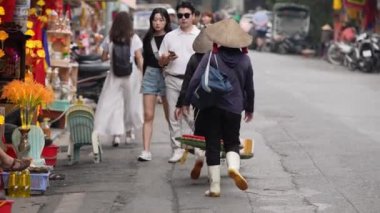 Vietnam, -05 Nisan 2024: Vietnamlı bir kadının yavaşlaması Hanoi Eski Mahallesi 'nde bir cadde boyunca yürüyor, geleneksel Asya konik hasır şapkası takıyor, Vietnam kültür mirasının simgesi..