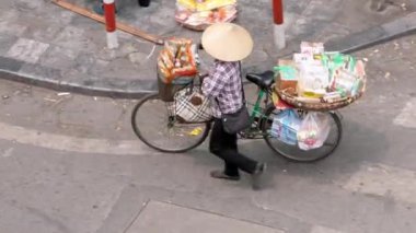 Vietnam, -04 Nisan 2024: Vietnam Hanoi Eski Mahallesi 'nde hava manzaralı, geleneksel Asya konik hasır şapkalı bir kadın cadde boyunca bisiklet sürüyor. Kültür mirası ve yerel kültürün temsilcisi