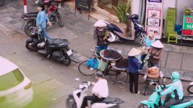 Vietnam, -04 Nisan 2024: Geleneksel Asya konik hasır şapkası takmış Vietnamlı bir sokak satıcısının hava görüntüsü, bisikletini Hanoi 'de bir yol boyunca mobil yiyecek tezgahı olarak kullanıyor.