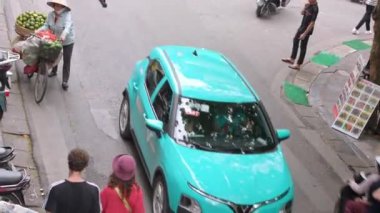 Vietnam, -04 Nisan 2024: Geleneksel Asya konik hasır şapkası takan Vietnamlı kadın hava görüntüsü, sokakta satmak için yeşil meyvelerle bisiklete biniyor.