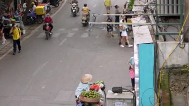 Vietnam, -04 Nisan 2024: Vietnamlı bir sokak satıcısının havadan görünüşü bisikletinde tropik meyve çeşitleri sunarken Asya konik hasır şapka takıyor. Kültür Mirası