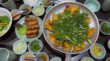 Vietnam usulü kızarmış börek Nem Ran, bir tabak kemiksiz ızgara hemibagrus balığı, Cha Ca La Vong Hanoi adında nehir yayın balığı, taze dereotu ve taze soğanlı yemek masası, kişniş,
