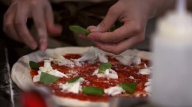 Eller titizlikle pizza hamuruna peynir ve fesleğen yaprağı ekler. İtalyan mutfağının özü, taze mozzarella ve otlarla hamuru lezzetli bir yemeğe dönüştürüyor..