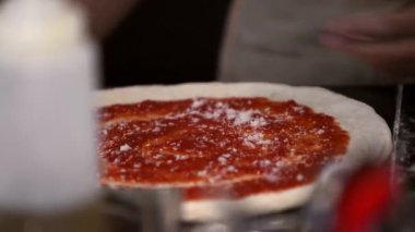 Bir şef titizlikle pizza hamuruna domates sosu ve peynir ekler. Taze mozzarella ile yapılan bu İtalyan pişirme işlemi hamuru lezzetli bir yemeğe dönüştürür..