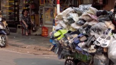 Vietnam, Hanoi-03 Nisan 2024: Geleneksel konik hasır şapka giyen bir sokak satıcısının yavaşlaması, ayakkabı dolu bir arabayı itiyor, Vietnam Eski Çeyreği 'ndeki bir yolda yol alıyor.