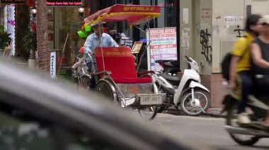 Vietnam, Hanoi-04 Nisan 2024: Hareketli şehir manzarasında, Vietnamlı bir sokak satıcısı temizlik ürünleri ve süpürge dolu bir bisikleti sürüp yol boyunca mobil bir kabine dönüştürüyor.