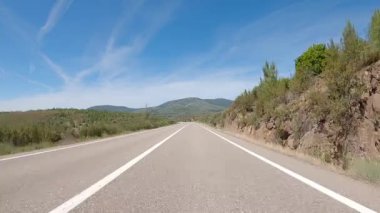POV driving a car on empty asphalt road through fields outside the city of spanish village during sunny day. Traffic ways transportation countryside concept.