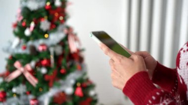 Noel tatili, telefonuyla mesajlaşan bir kadın, bereketli bir yaşam tarzının tadını çıkarırken, yemyeşil çam ağacının arka planında Noel ağacı Xmas ile çevrili..