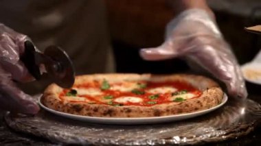 Bir şef profesyonel bir mutfakta sıcak pizzayı metal bir tepside ustaca keser. Bıçak mozzarellayı dilimliyor. Yaradılışın tepesinde, servis etmeye hazır hale getiriyor..