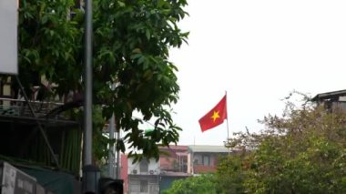 Kızıl Vietnam bayrağının yavaşlaması, güçlü bir ulusal sembol, Hanoi şehrinde bir caddede yüksekte dalgalanır, ülke kimliğini, mirasını ve gururunu temsil eder..