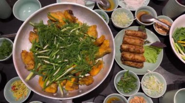 Vietnam usulü kızarmış börek Cha Gio, bir tabak kemiksiz ızgara hemibagrus balığı, Cha Ca La Vong Hanoi adında nehir yayın balığı, taze dereotu ve taze soğanlı restoranlar masası, kişniş,