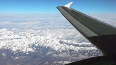 Uçak penceresinden uçarken kanat çırpıyor, Alpler karla kaplanıyordu, engebeli dağ zirveleri manzarayı kaplıyordu. Üst katlar hafif kar tozlarıyla kaplı.