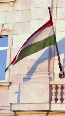 Macaristan 'ın Budapeşte kentindeki bir binanın cephesinde sallanan Macaristan bayrağının dikey yavaş hareketi. Ulusal gurur, kültürel kimlik ve şehir manzarasını sembolize eder..