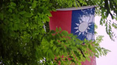 Tayvan bayrağının yavaş hareketi canlı yeşil yapraklarla kısmen gizlenerek ulusal kimliğin ve doğanın sembolik bir görünümünü oluşturuyor..