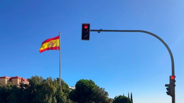 Spanish flag waving proudly next to a red traffic light against a clear blue sky. Captures urban scenery and patriotism in a single frame. clipart