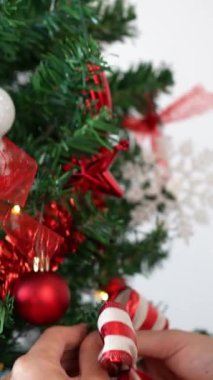 Dikey Kadın Noel ağacını güzel kırmızı ve beyaz fiyonkla süslüyor. Noel kurdelesiyle süslenmiş bir kız Xmas süsleri. Yeni yıl dekorasyon ögesi