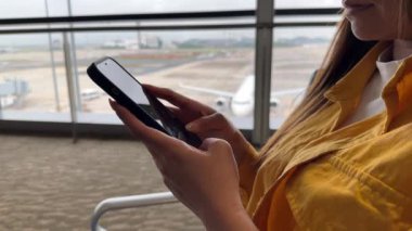 Sessiz ve modern bir havaalanı terminalinde akıllı telefondan seyir eden yolcu. Modern seyahat rutinlerinin özünü yakalıyor. Teknoloji ve seyahatin harmanlandığı mükemmel bir an..