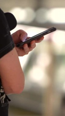 Dikey, Hands modern havaalanının terminalinde akıllı telefonu tutuyor. Yoğun bir ulaşım merkezinde seyahat ve bağlantının mükemmel bir tasviri. Teknoloji ve seyahat içeriği için kullanışlı.