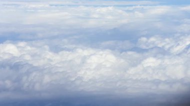 Pofuduk beyaz bulutların uçsuz bucaksız mavi gökyüzüne uzanan görüntüsü. Barışçıl atmosfer, doğa dokusunun güzelliğini yukarıdan vurguluyor.